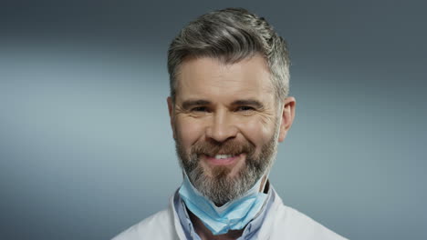 Portrait-of-the-young-Caucasian-happy-man-physician-taking-off-mask-from-his-mouth-and-smiling-cheerfully.-Close-up.